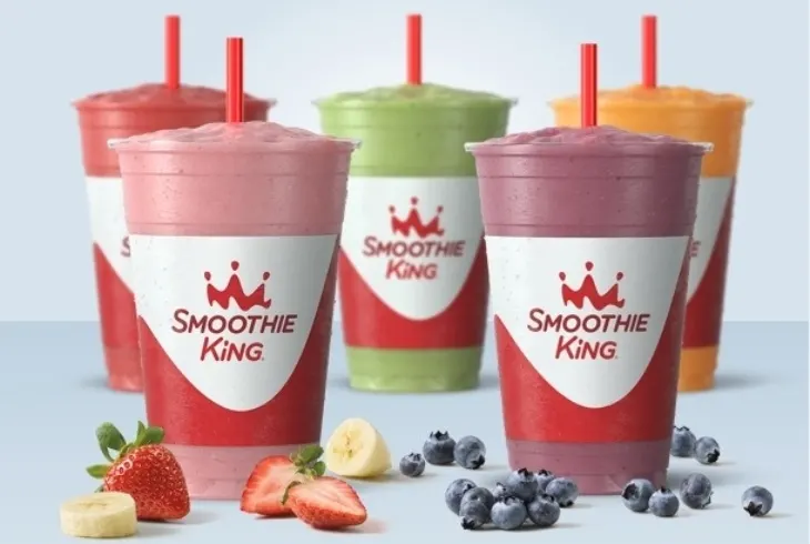 five colorful smoothies in red and white Smoothie King cups with fresh fruit.