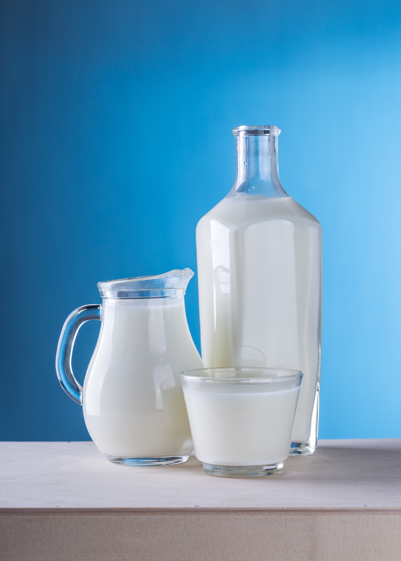 a glass pitcher, a tall bottle, and a short glass all full of white milk.