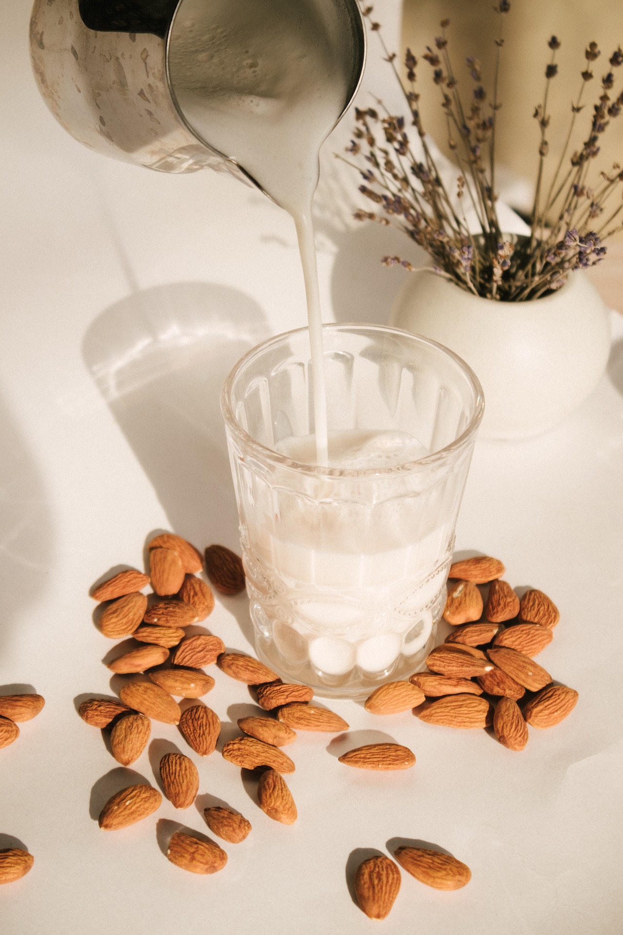 a glass of almond milk being poured surrounded by whole almonds.