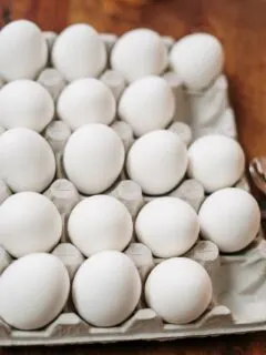 a large carton of white eggs on a wooden table.