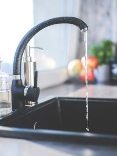 a black kitchen sink and faucet with the water running.