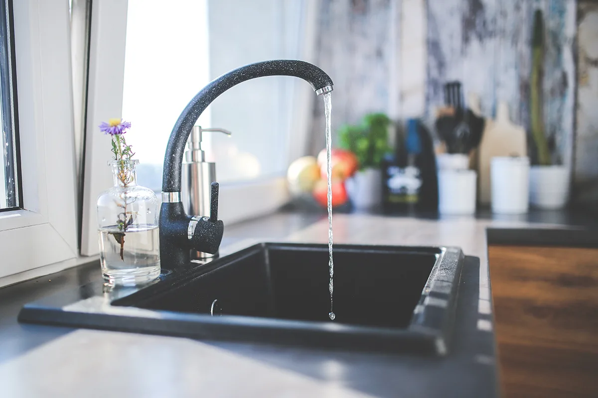 water running from a curved black faucet in a sunny kitchen.