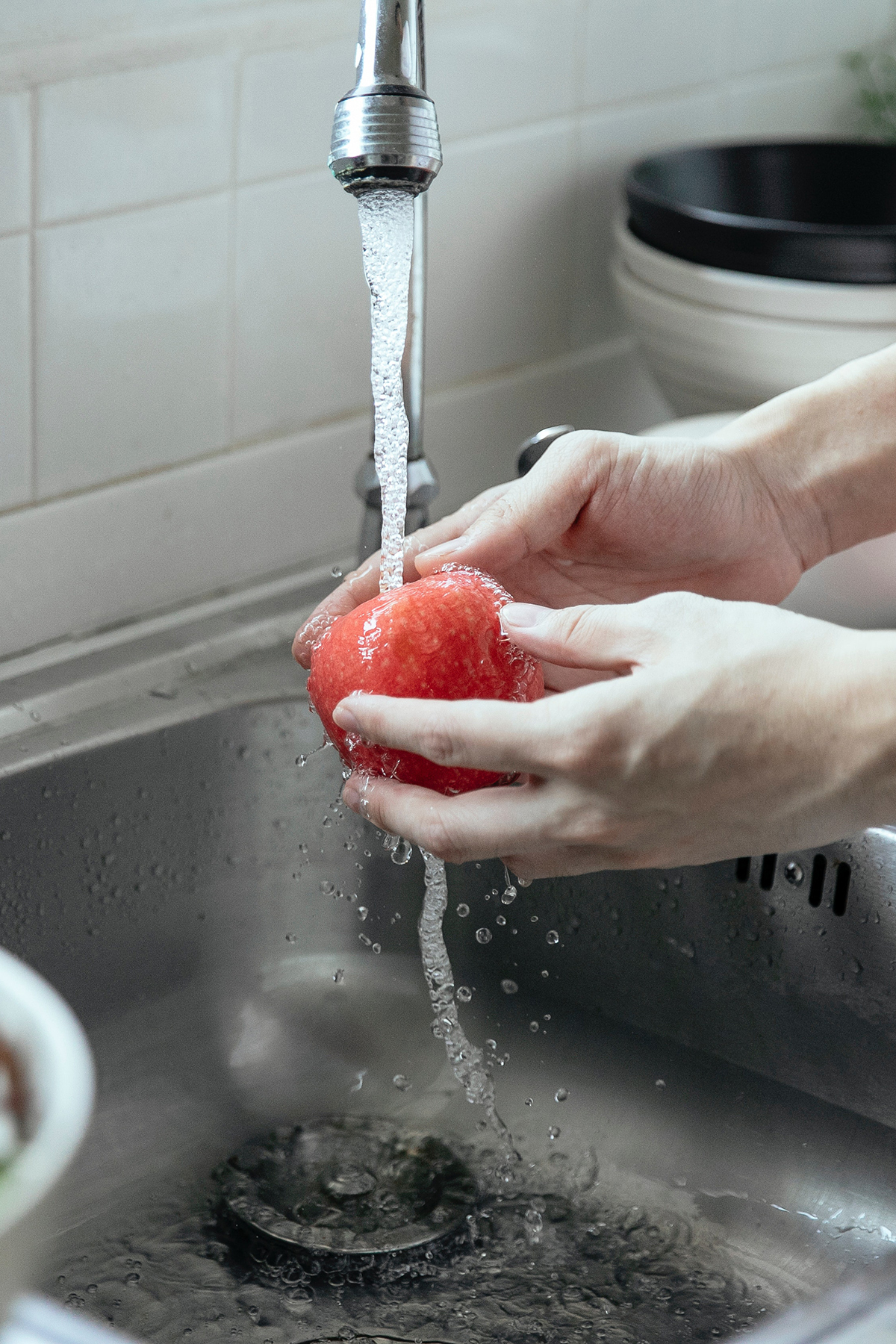 hands washing an apple in a silver kitchen sink.
