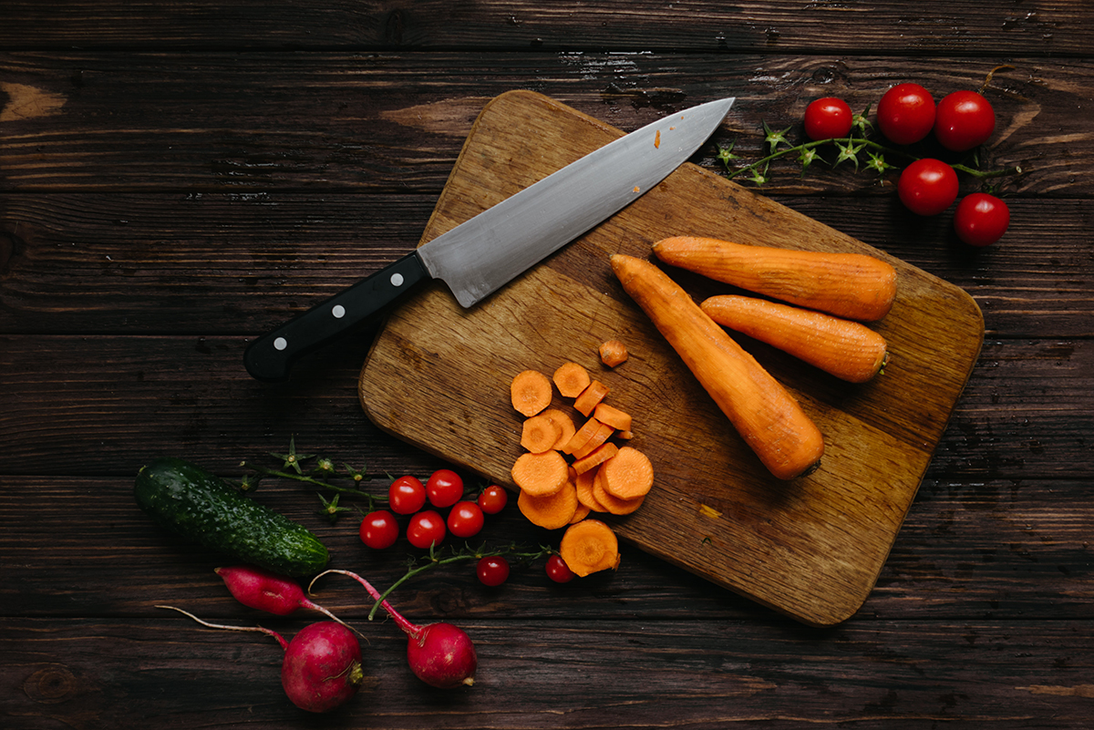 a kitchen knife on a cutting board with carrots.