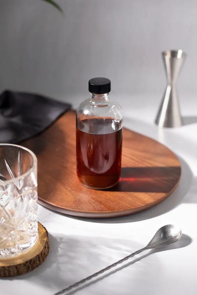 a bottle of demerara simple syrup next to bar tools and a rocks glass.