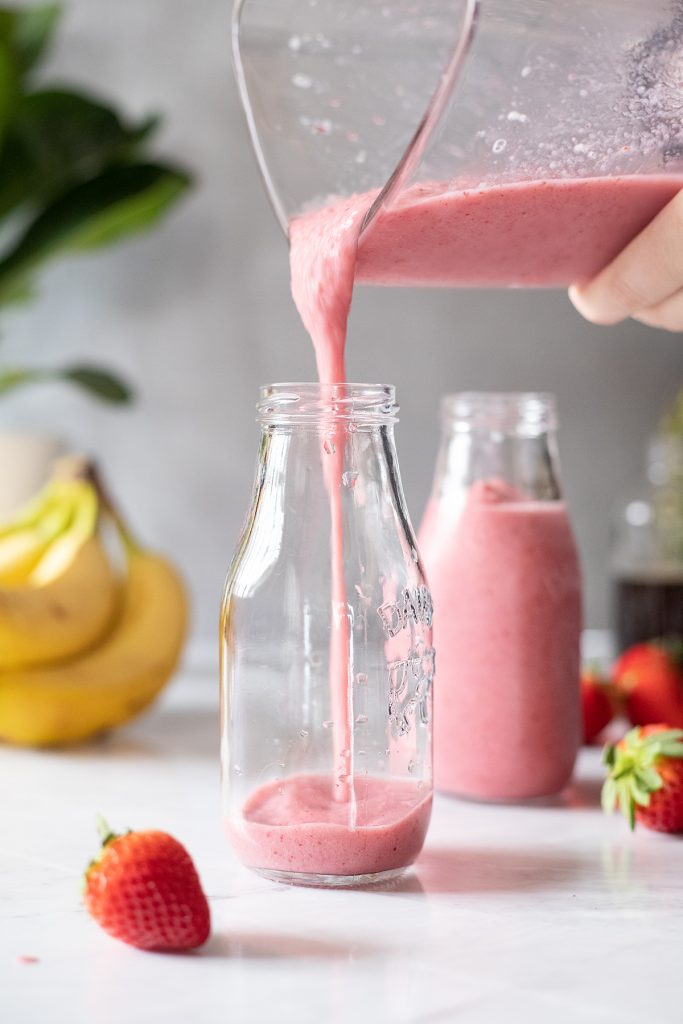 pouring a pink smoothie from blender into a glass milk bottle.