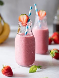 two glass bottles filled with pink, creamy smoothies and blue straws.