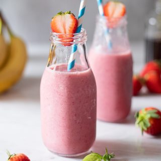 two glass bottles filled with pink, creamy smoothies and blue straws.