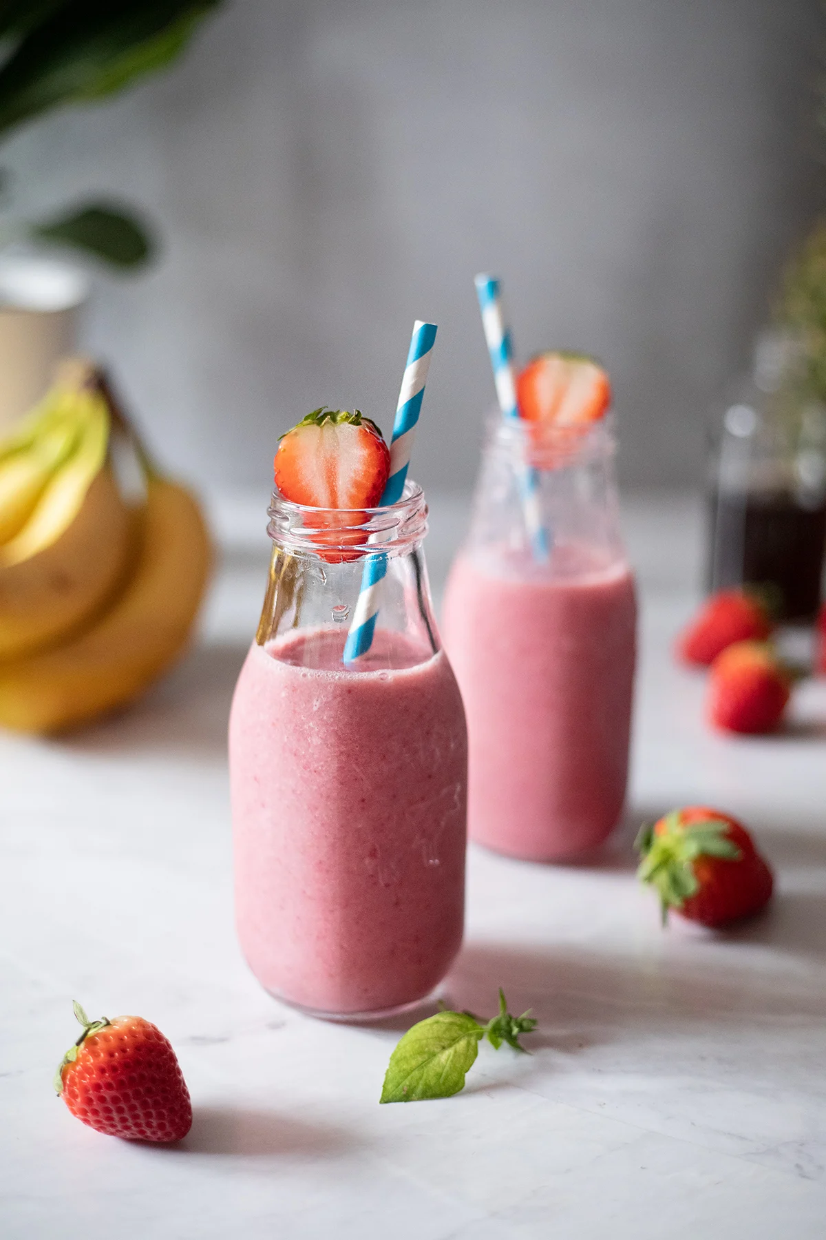 two pink smoothies in glass milk bottles with blue paper straws.