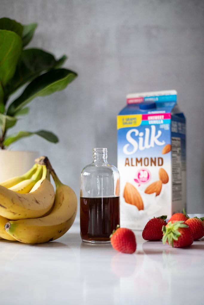 a bunch of bananas, some strawberries, a carton of almond milk, and a bottle of simple syrup.