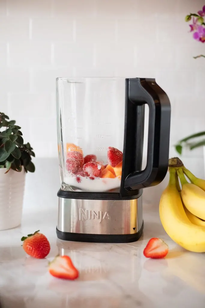 a Ninja blender filled with strawberries and almond milk.