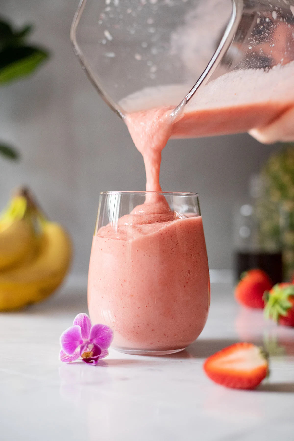 pouring a pink smoothie into a stemless wine glass.