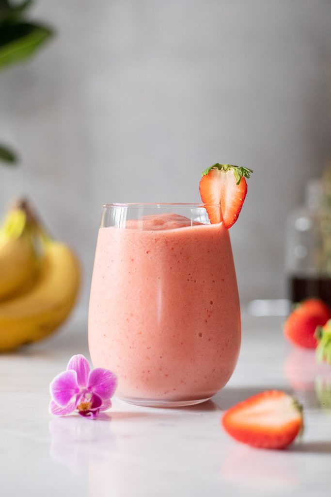 a short glass filled with a creamy pink smoothie with strawberries and a flower.