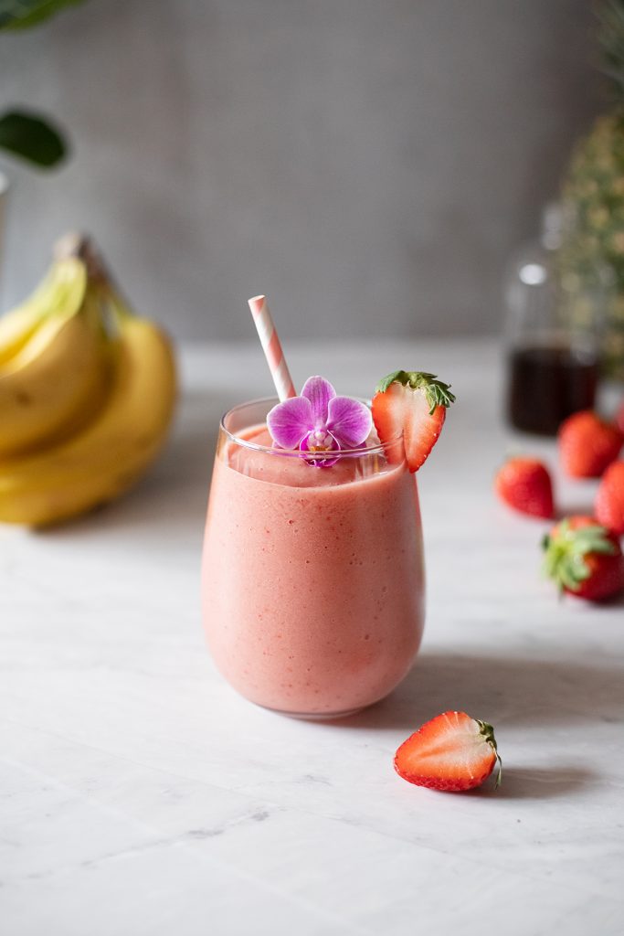 a pink smoothie with a straw next to bananas and strawberries.