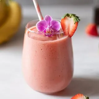 a glass filled with a pink smoothie and garnished with a strawberry and a purple flower.