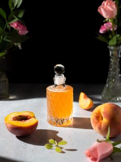 an antique glass bottle filled with pale orange syrup next to peaches.