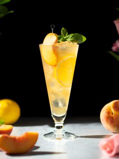 a glass of peach green iced tea garnished with a peach slice and basil leaves.