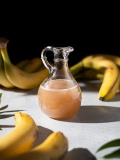 a glass pitcher of banana syrup next to ripe bananas.