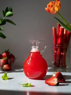 a bottle of bright red strawberry rhubarb simple syrup.