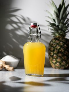a bottle of bright yellow syrup next to a pineapple and ginger root.