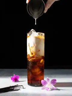 a tall glass of iced coffee with cream floating on top.