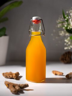 close up of a bottle of turmeric syrup next to turmeric roots.