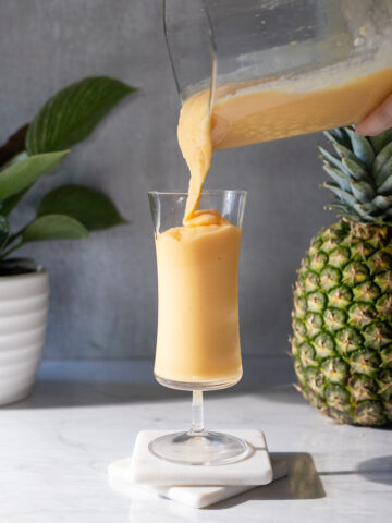 pouring a thick orange smoothie into a tall glass.