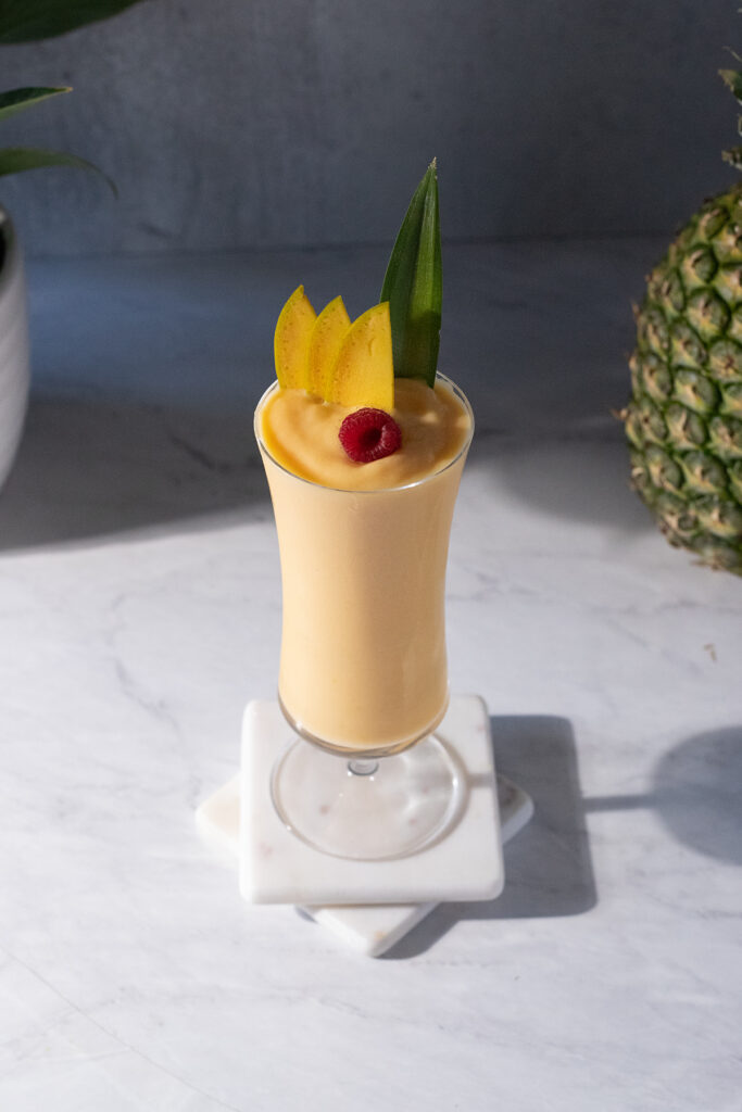 an orange smoothie with mango slices on a white marble countertop.