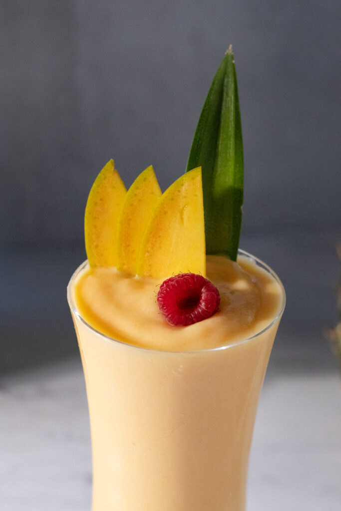 a close up of the top of an orange smoothie garnished with a raspberry and mango slices.