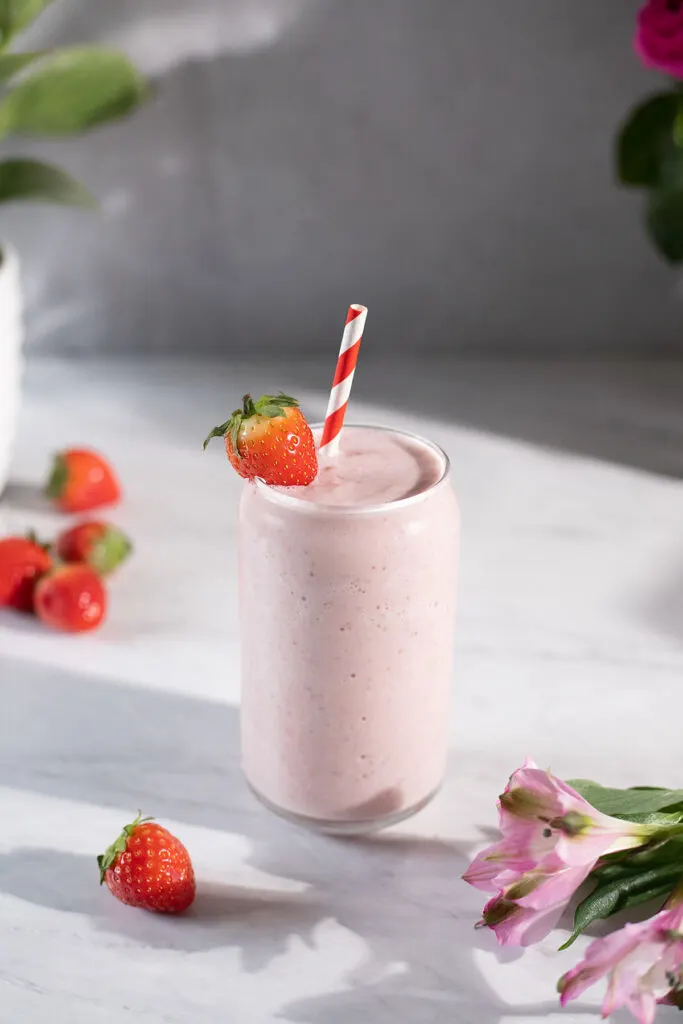 a pale pink, creamy smoothie in a can-shaped glass with strawberries and pink flowers.