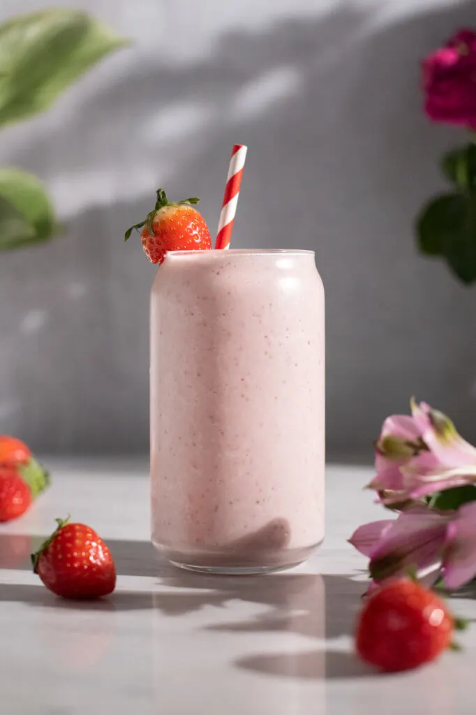 a tall glass filled with a pale pink creamy smoothie and topped with a strawberry.