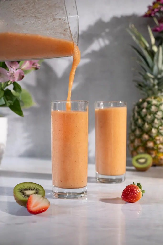 pouring an orange smoothie from blender into a tall glass.