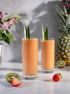 two orange smoothies with pineapple leaves in tall, skinny glasses.