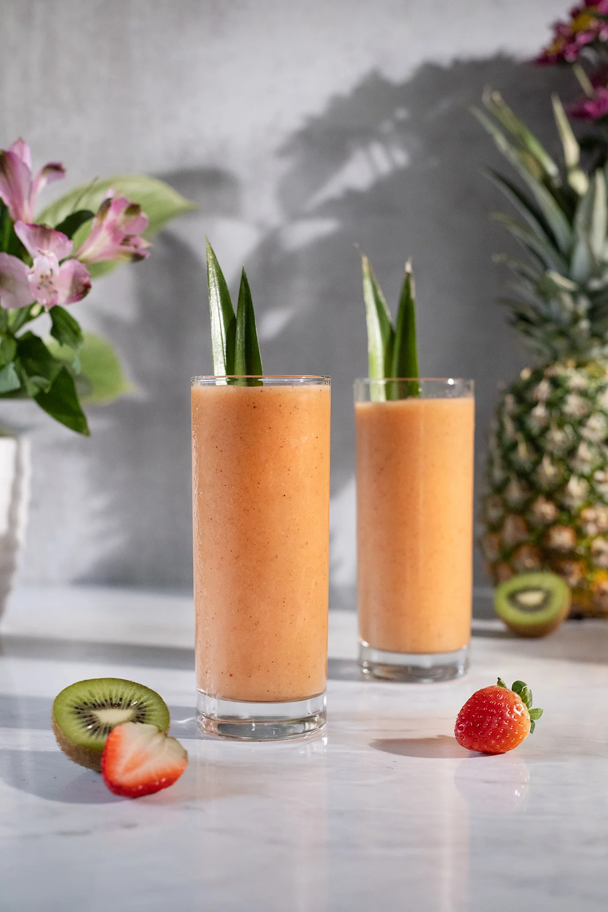 two orange smoothies with pineapple leaves in tall, skinny glasses.
