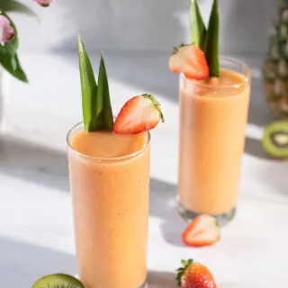 two orange smoothies in tall glasses garnished with pineapple leaves.