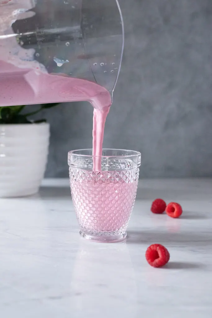 pouring a pink smoothie into a glass.