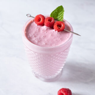 a glass filled with a creamy pink smoothie topped with raspberries.