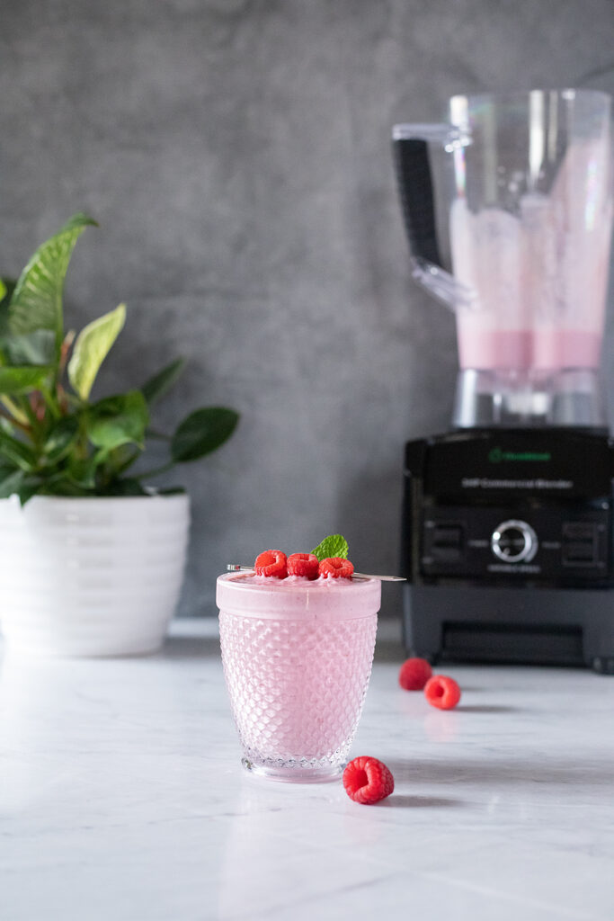 a pink smoothie with raspberries next to a blender.