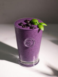 a tall glass filled with a purple smoothie topped with frozen blueberries.