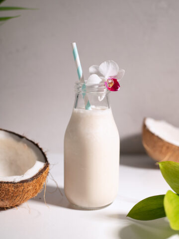 a white shake in a vintage-style milk bottle with a paper straw and white orchid.