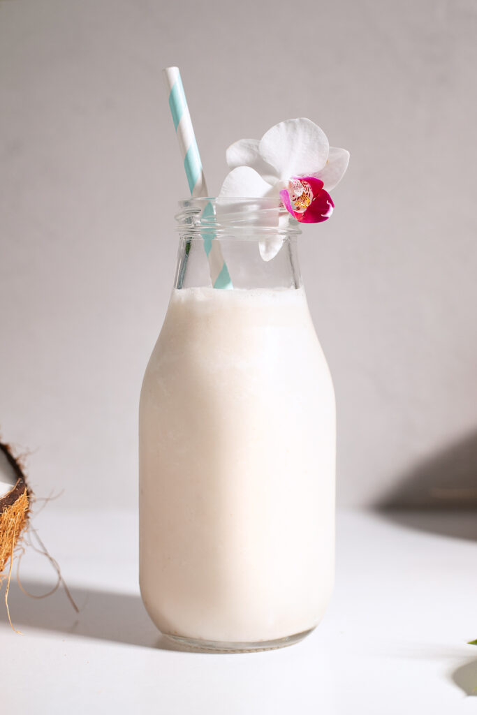 a white shake in a glass milk bottle with a blue paper straw and a white orchid.
