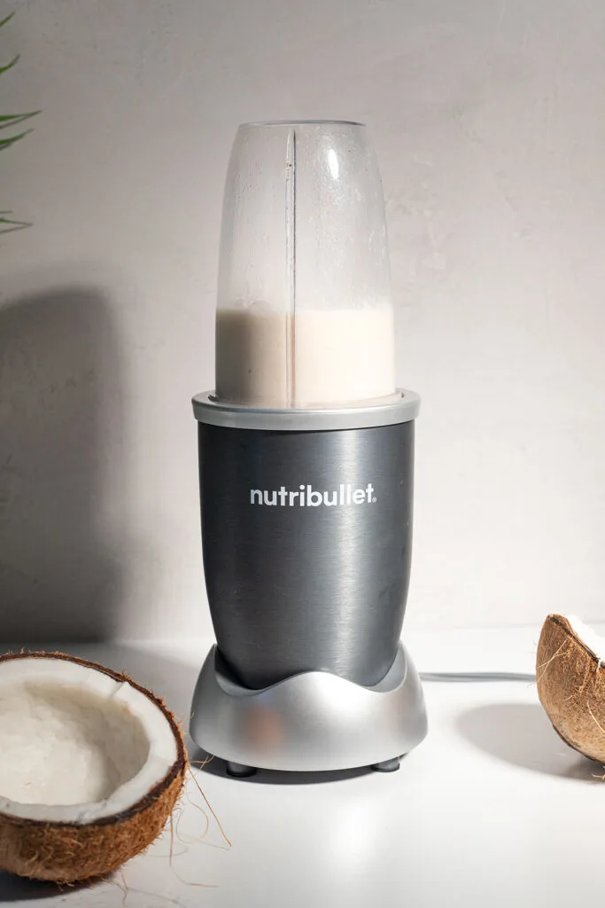 a nutribullet filled with a white liquid next to a coconut.