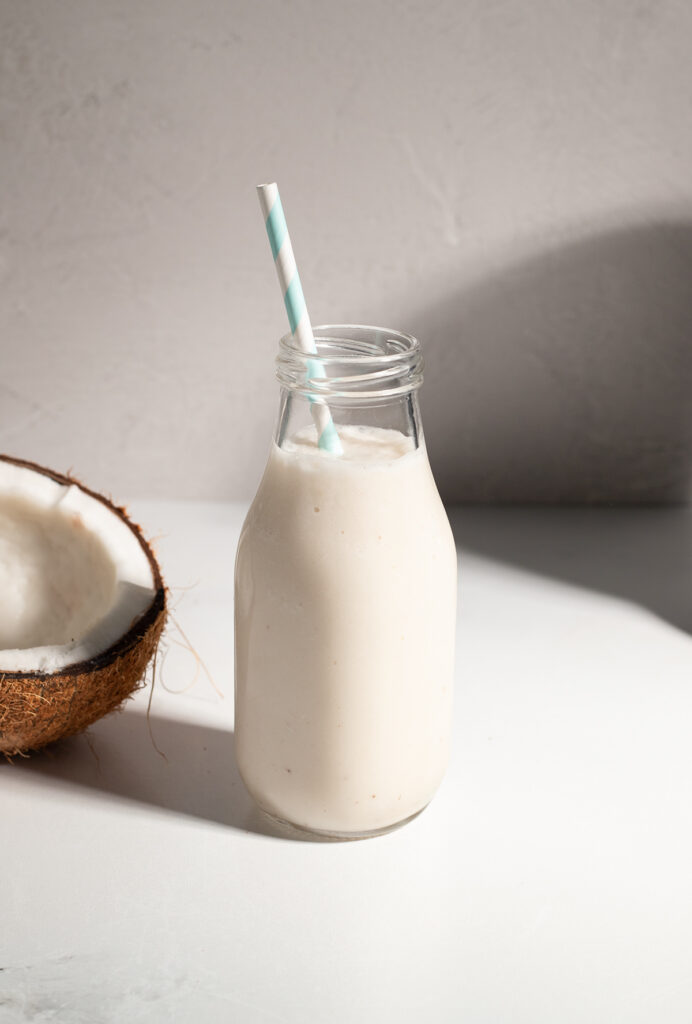 white liquid in a glass milk bottle next to a coconut.