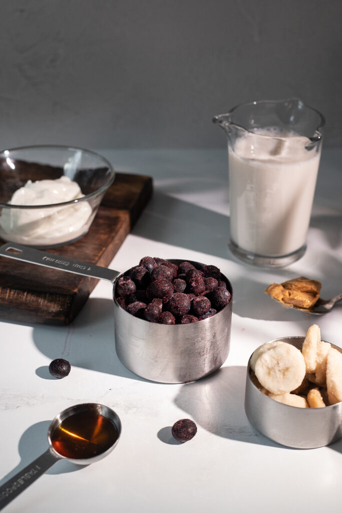 metal measuring cups with smoothie ingredients: frozen blueberries, yogurt, banana.