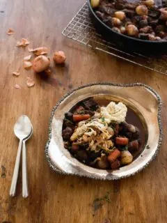 beef stew with potatoes in a silver bowl on a rustic wood table.