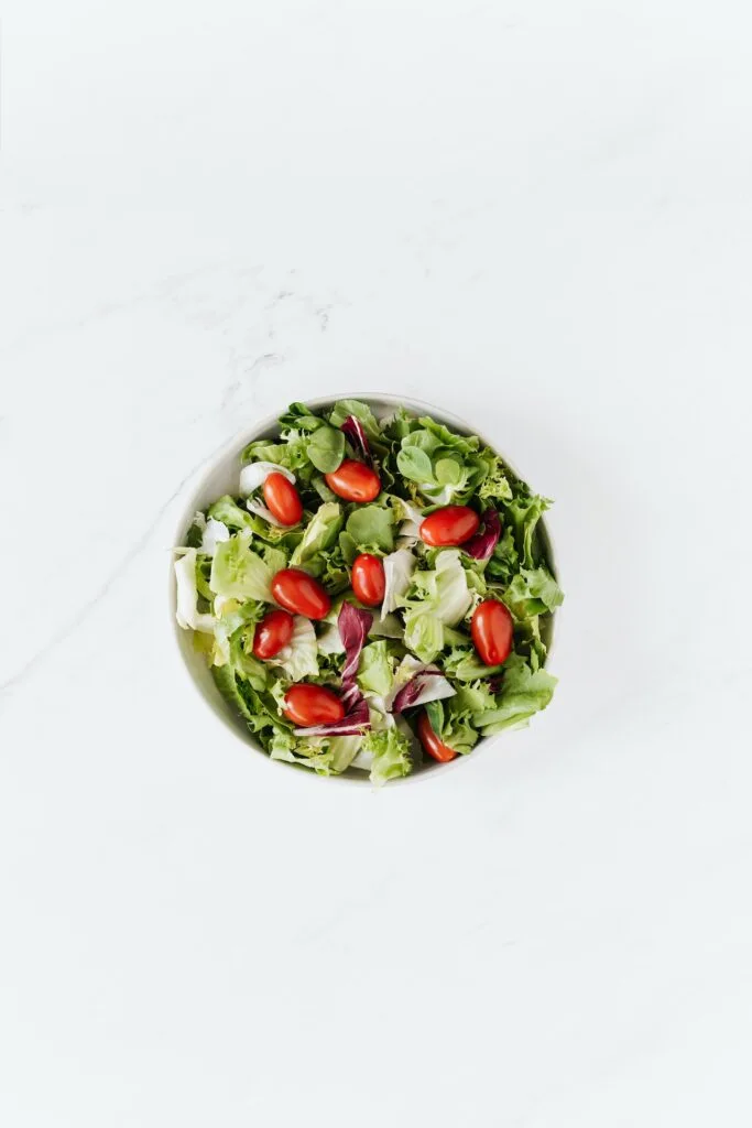 top down view of a salad with lettuce and grape tomatoes on a white table.