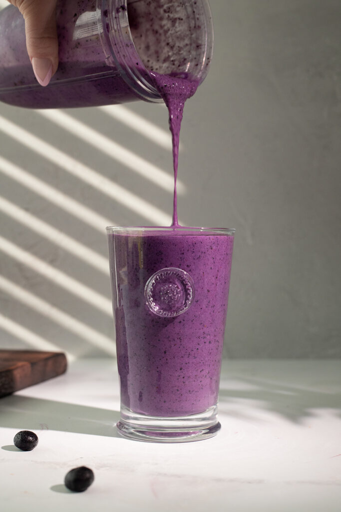 pouring a dark purple smoothie from blender into a tall glass.